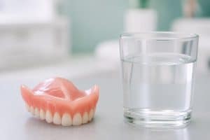 Proteză dentară totală lângă un pahar cu apă